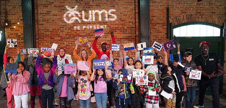 A group of children holding artwork standing in front of a brick wall.