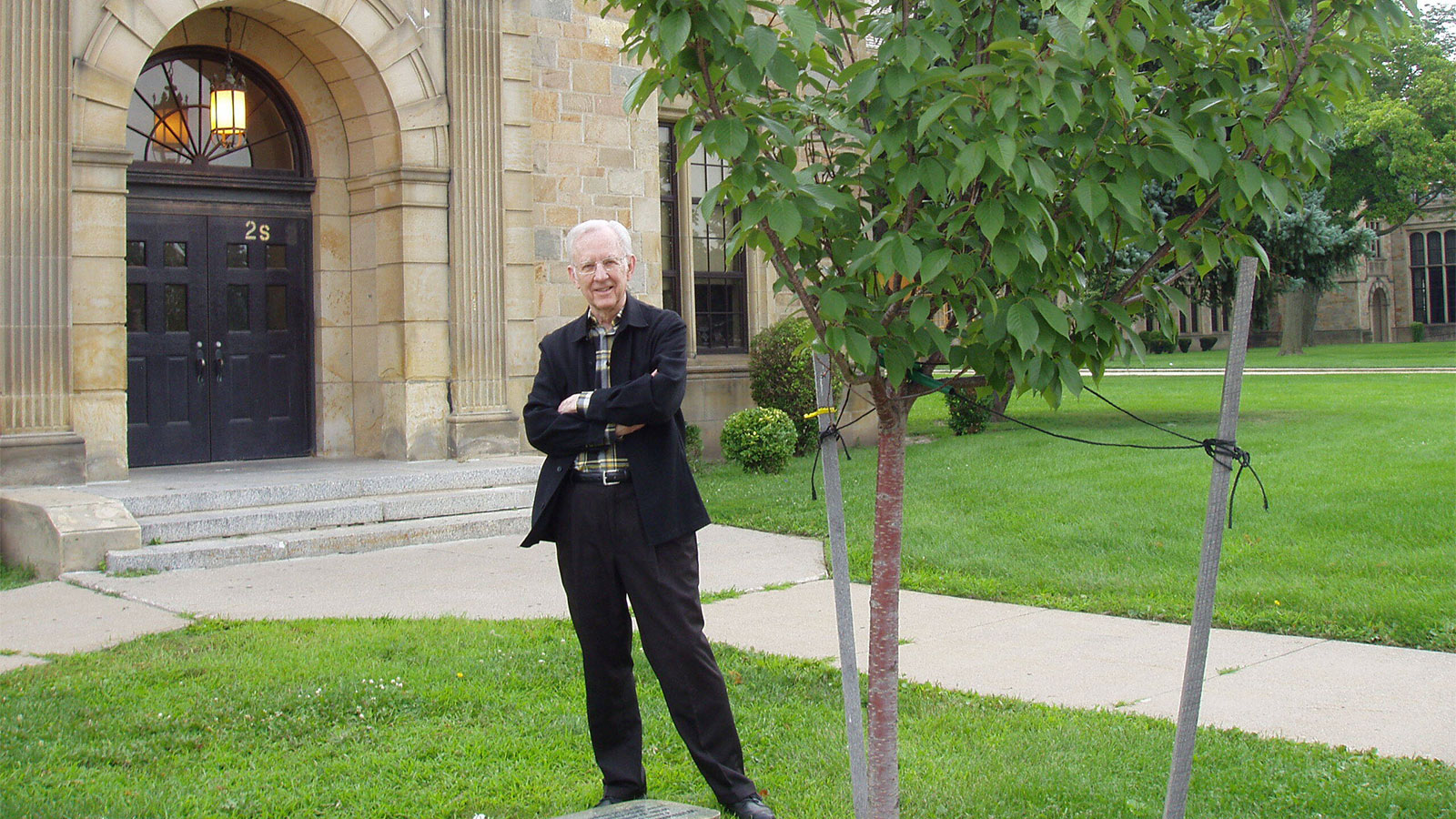 William Brehm standing with his arms crossed next to a tree on the lawn of Fordson High School.