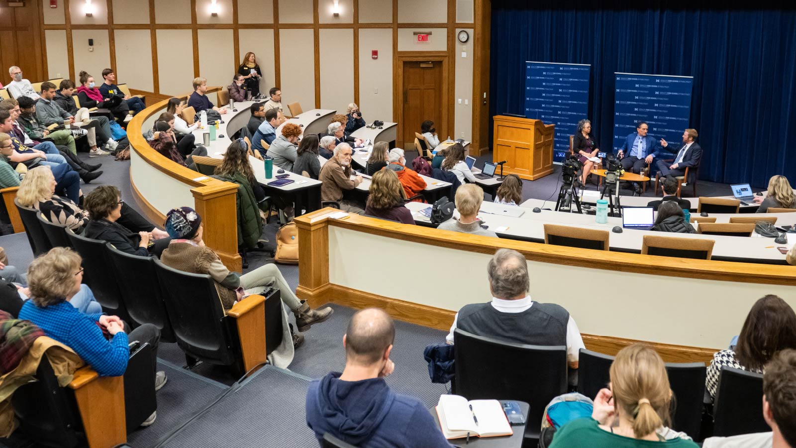 A group of people in a lecture hall listening to a panel discussion.