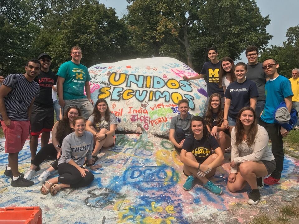 A group of students sitting on a large painted rock.