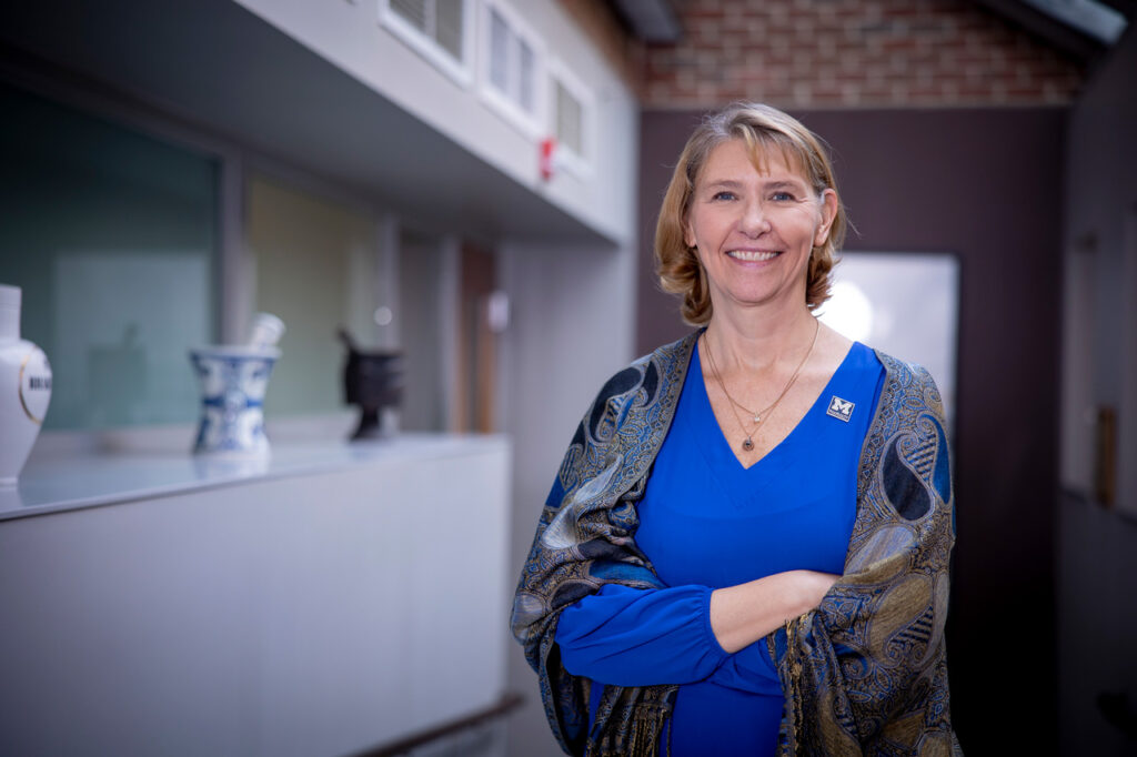 The College of Pharmacy Dean, Vicki Ellingrod, posing for a photo in a hallway with vases on the ledge behind her.