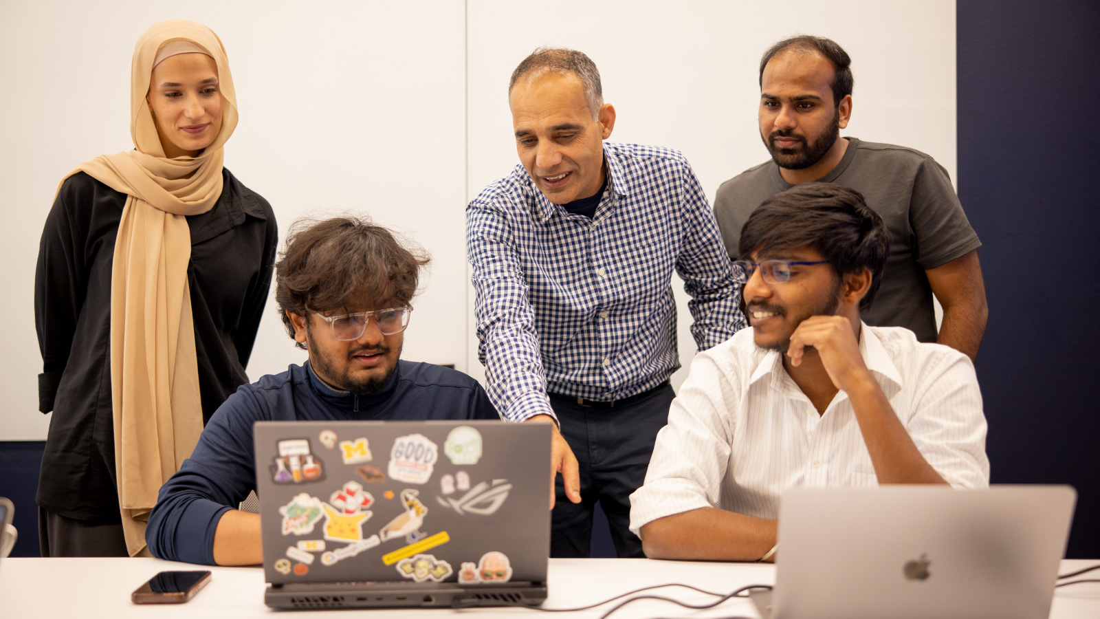 Hafiz Malik and a group of students are huddled together looking at a laptop computer.