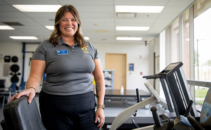 A portrait of Desiree Frantum standing next to an exercise bike, with a treadmill in the background.