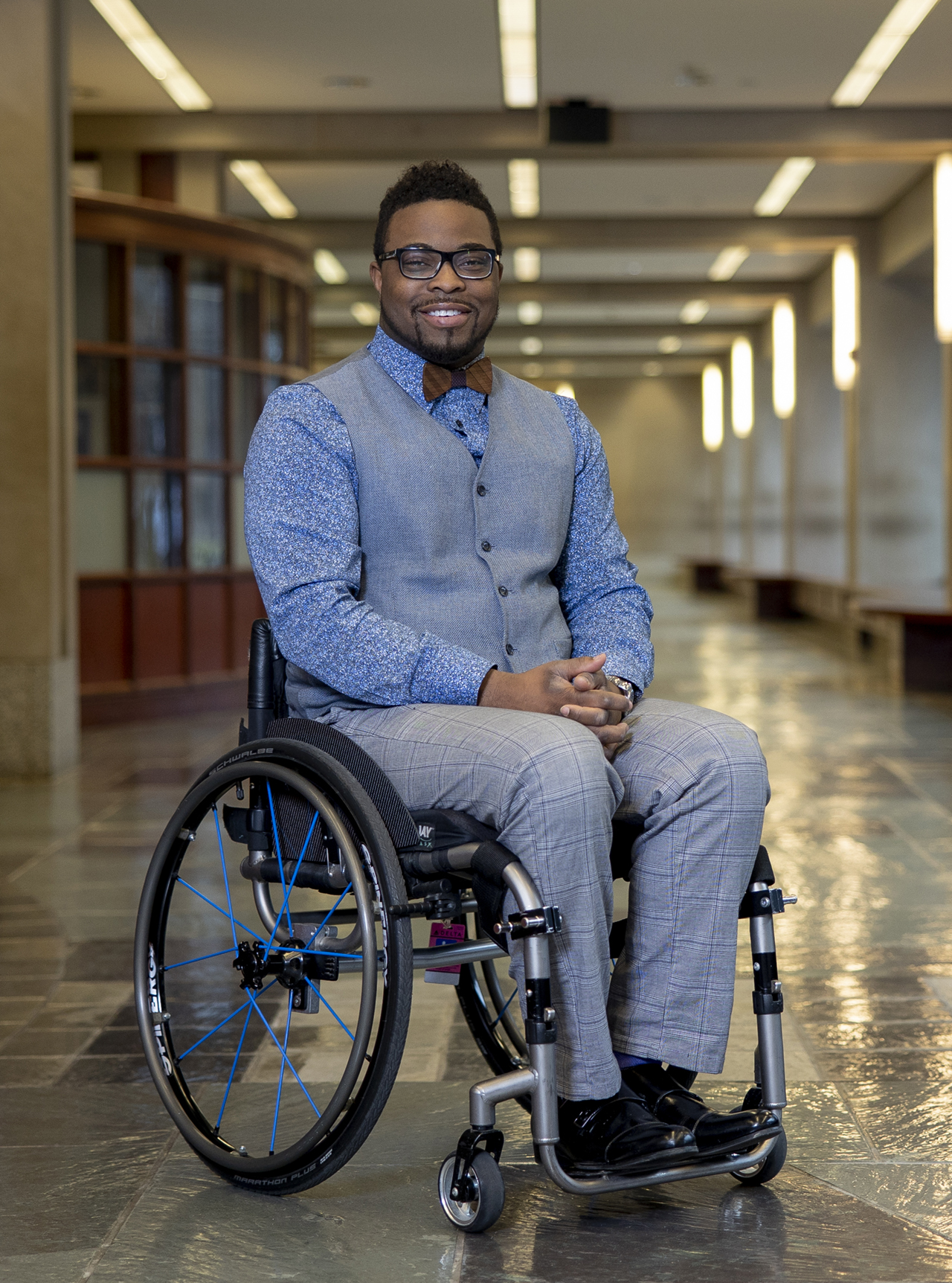 Dr. Oluwaferanmi Okanlami sitting in his wheelchair, posing for a photo in a hallway.