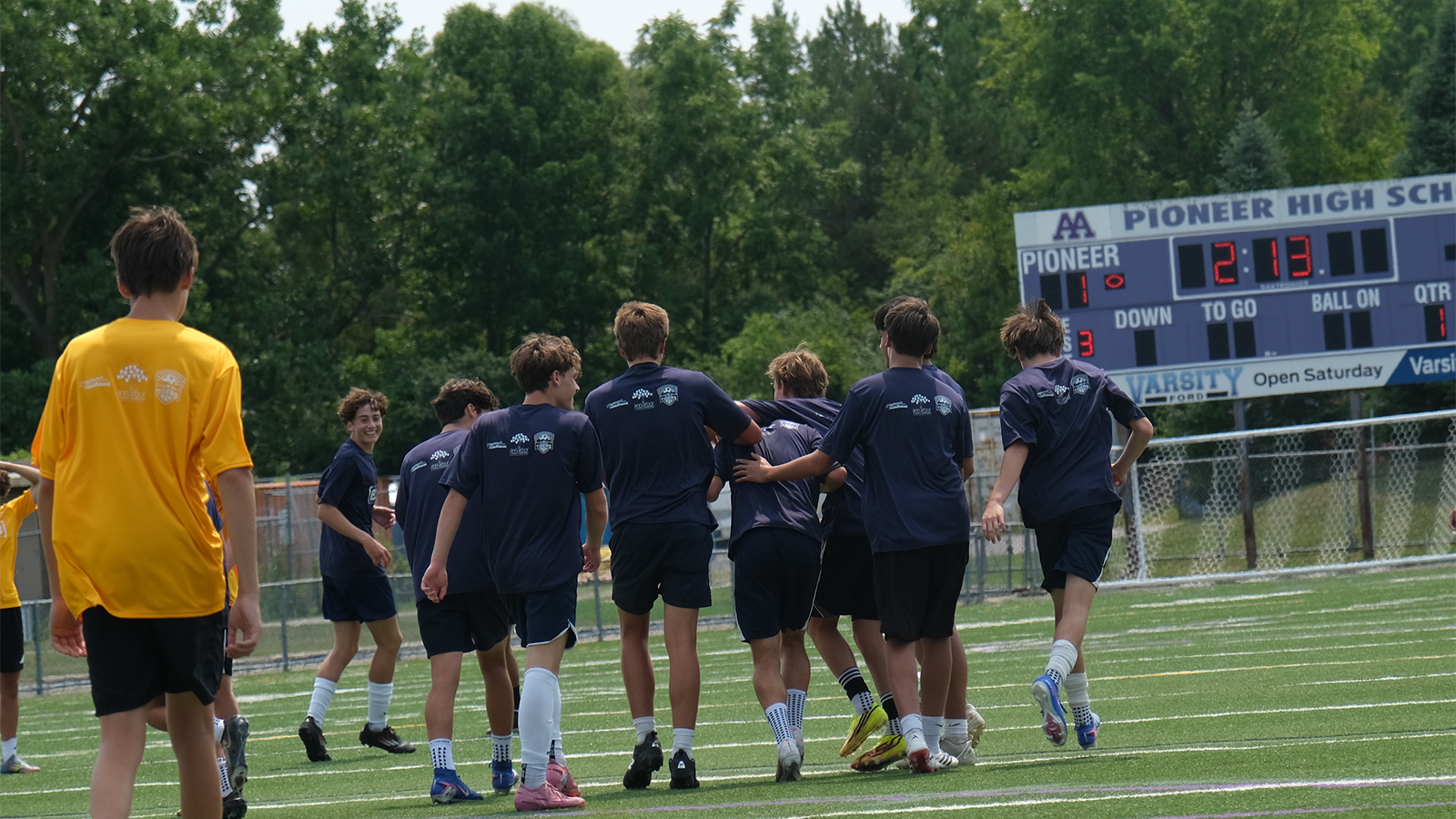 Elliott and fellow soccer players at his charity game on a field in front of the Pioneer High School scoreboard. 