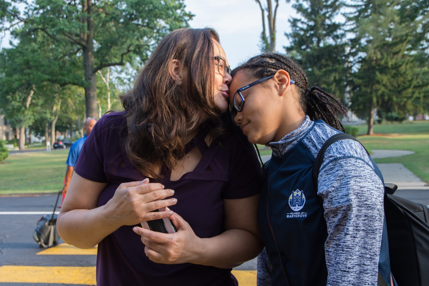 A woman kissing a girl's forehead on the first day of school.