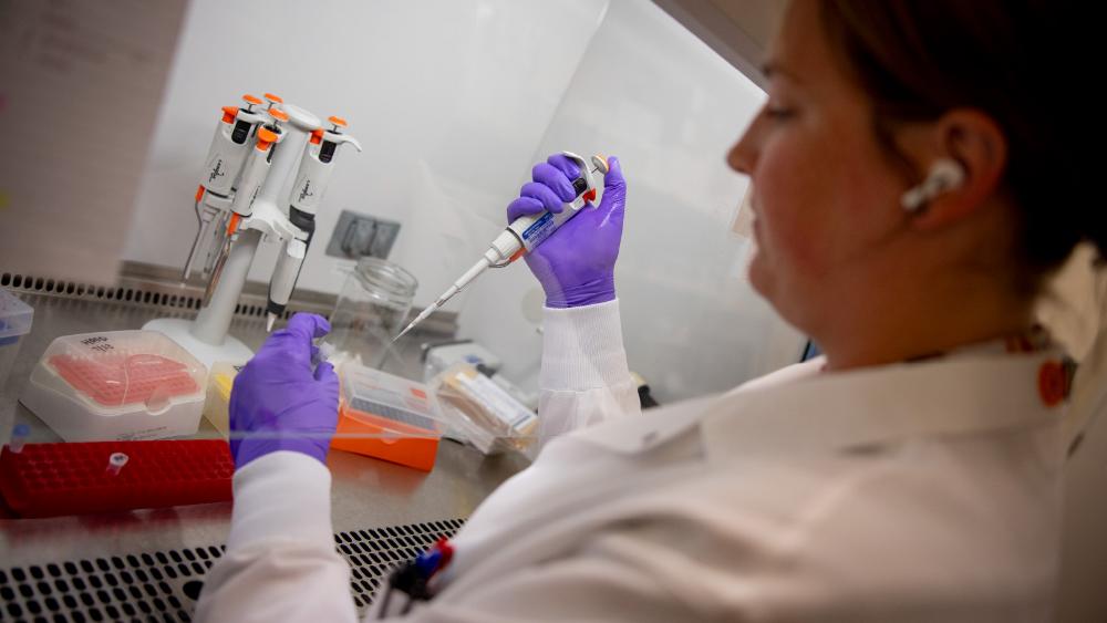 A student wearing a lab coat and purple surgical gloves holding an instrument in a lab.