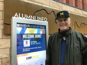 John Madigan, stands next to a welcome screen during a campus visit.