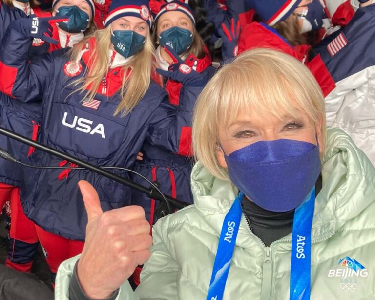 Joyce gives a thumbs up in front of a group of people wearing Team USA jackets. 