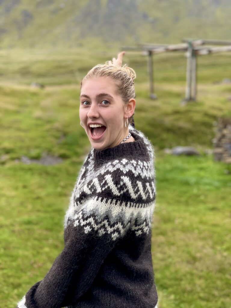 Julia in a field pointing to the landscape behind her.