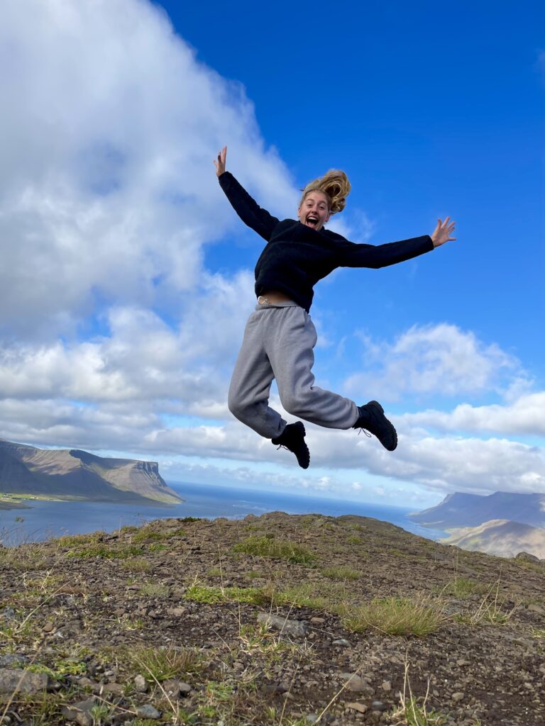 Julia jumping in the air on a mountain top overlooking a fjord.