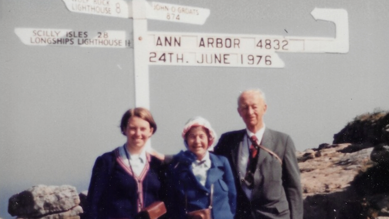 Two women and one man standing together outside in front of an arrow sign