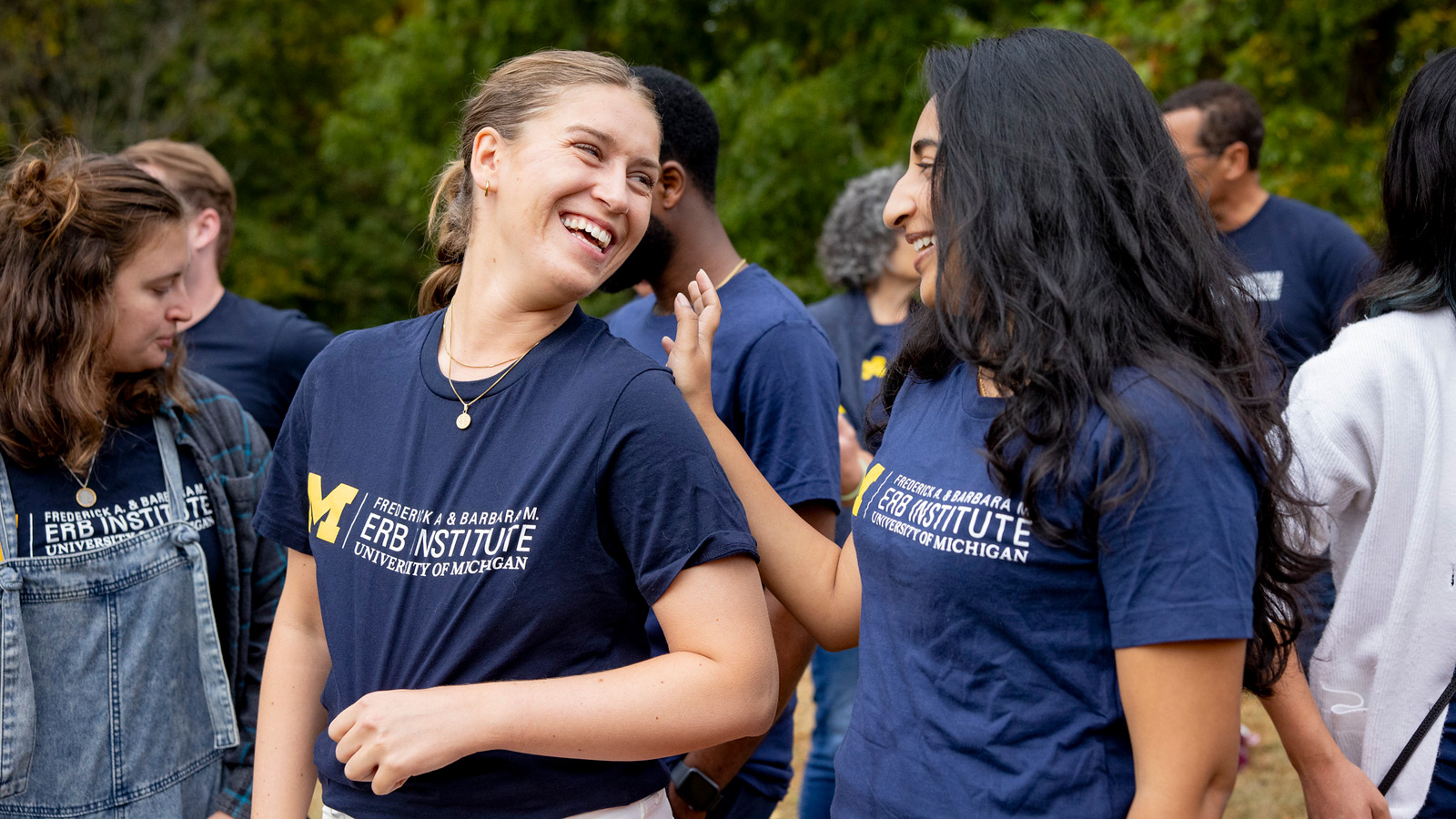 Two women laugh together at an outdoor gathering while wearing matching navy Erb Institute t-shirts.