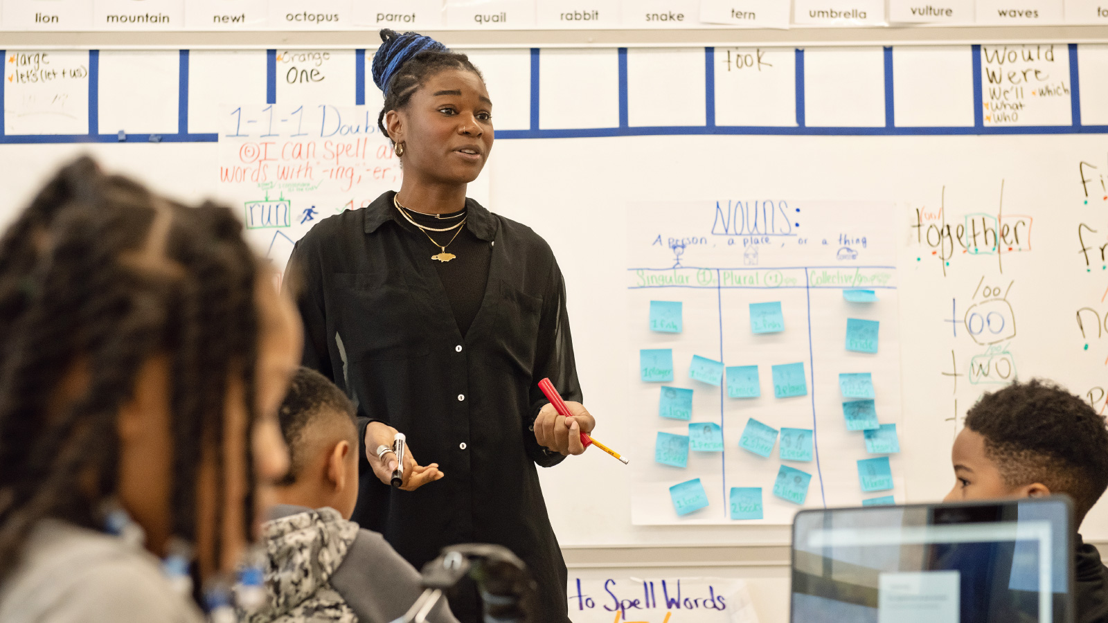  A teacher standing in front of a whiteboard with students sitting at desks.