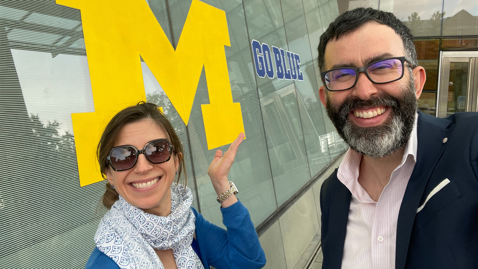 A photo of Marie-Lise Perrault and Miguel Andrés Sossa-Mardomingo (MBA, MS ’13) in front of a wall with the Michigan Block M and Go Blue.