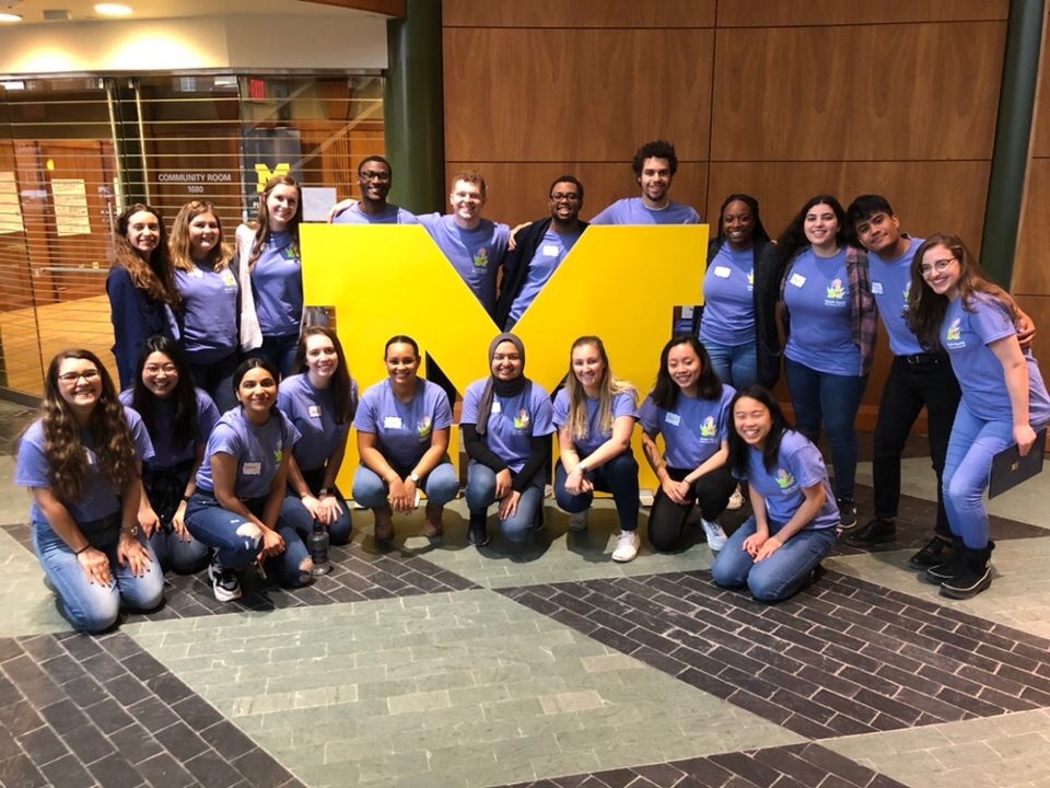 Group of students pose around a large block M at a research symposium.