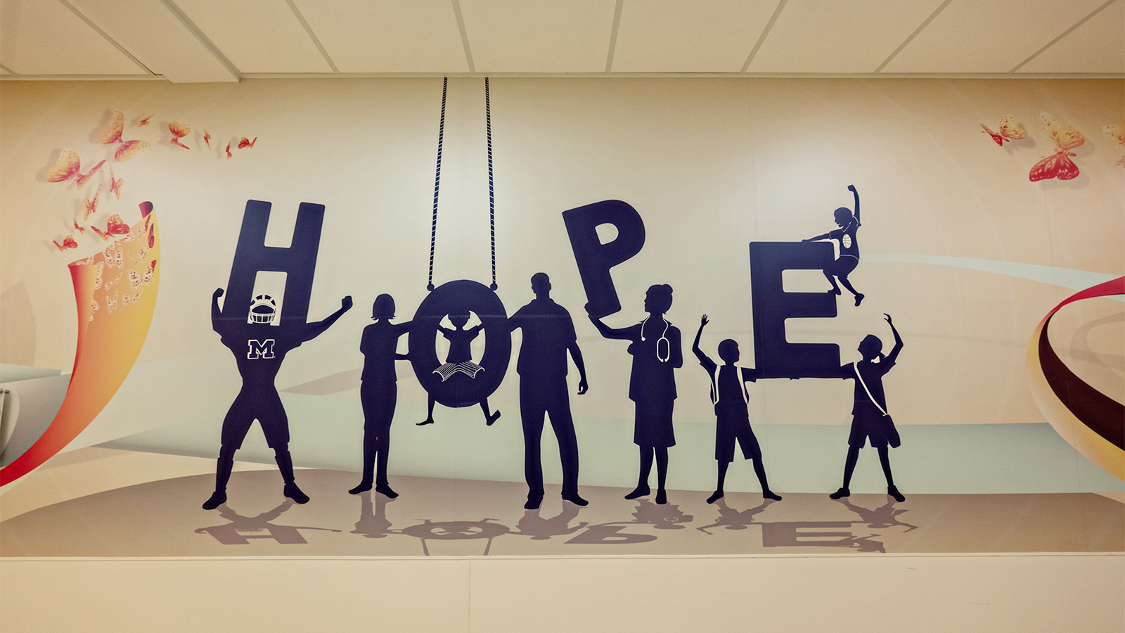 Silhouettes of children and adults holding letters that spell “HOPE,” featuring playful accents and Michigan-themed imagery.