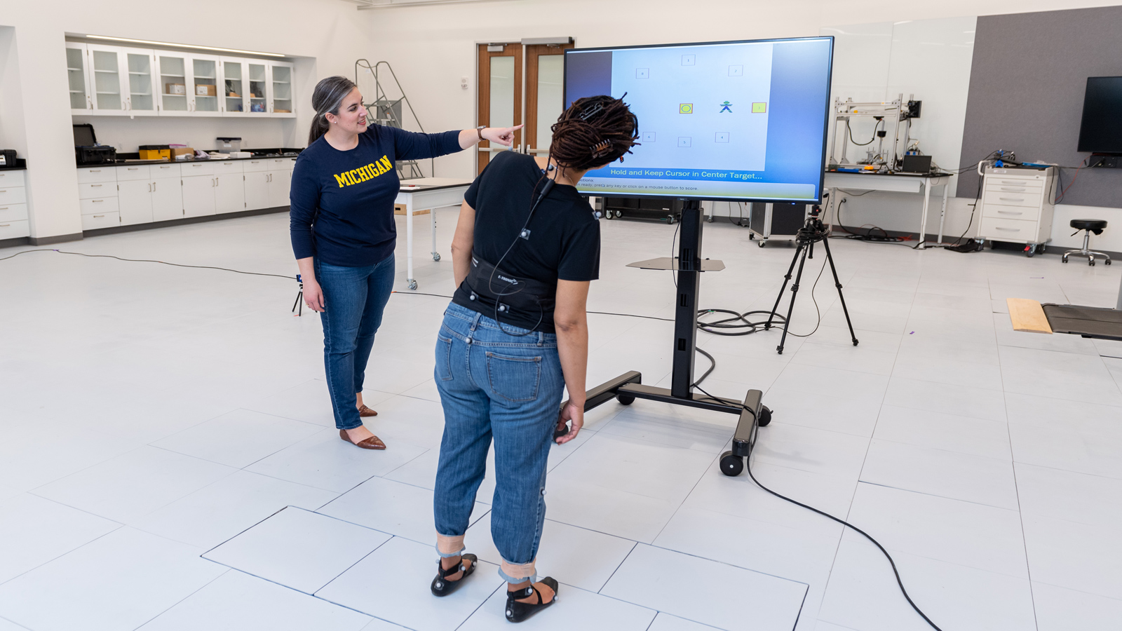 Two people stand in a modern lab. The lab is equipped with desks, computers, and other technical devices.