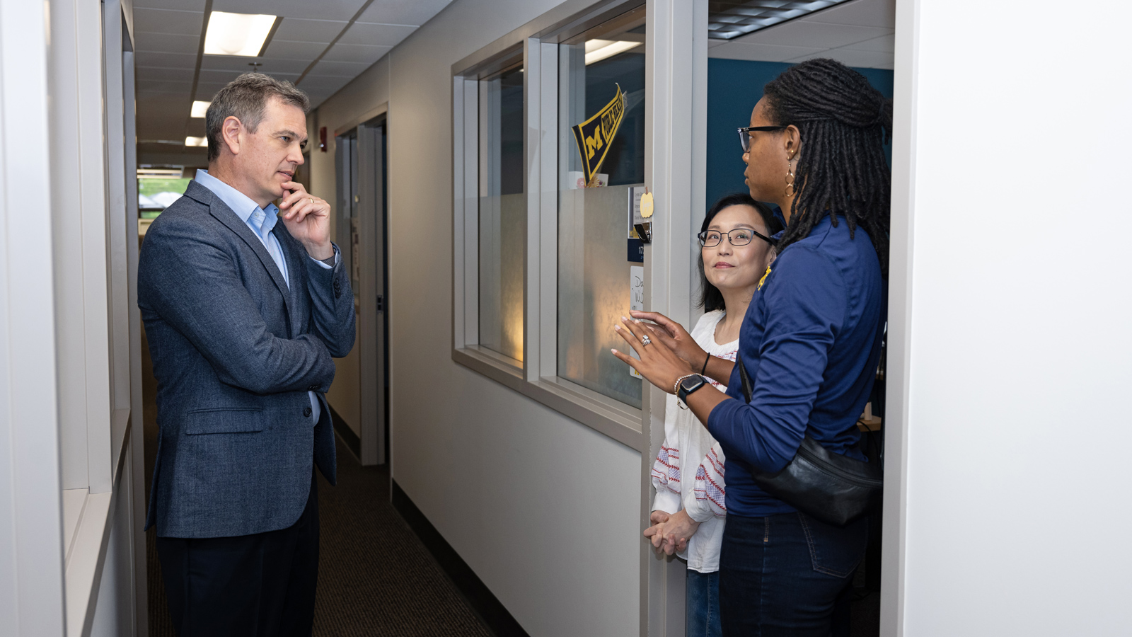 Dean Charles Holmes listens attentively to two faculty/staff members in a hallway.   