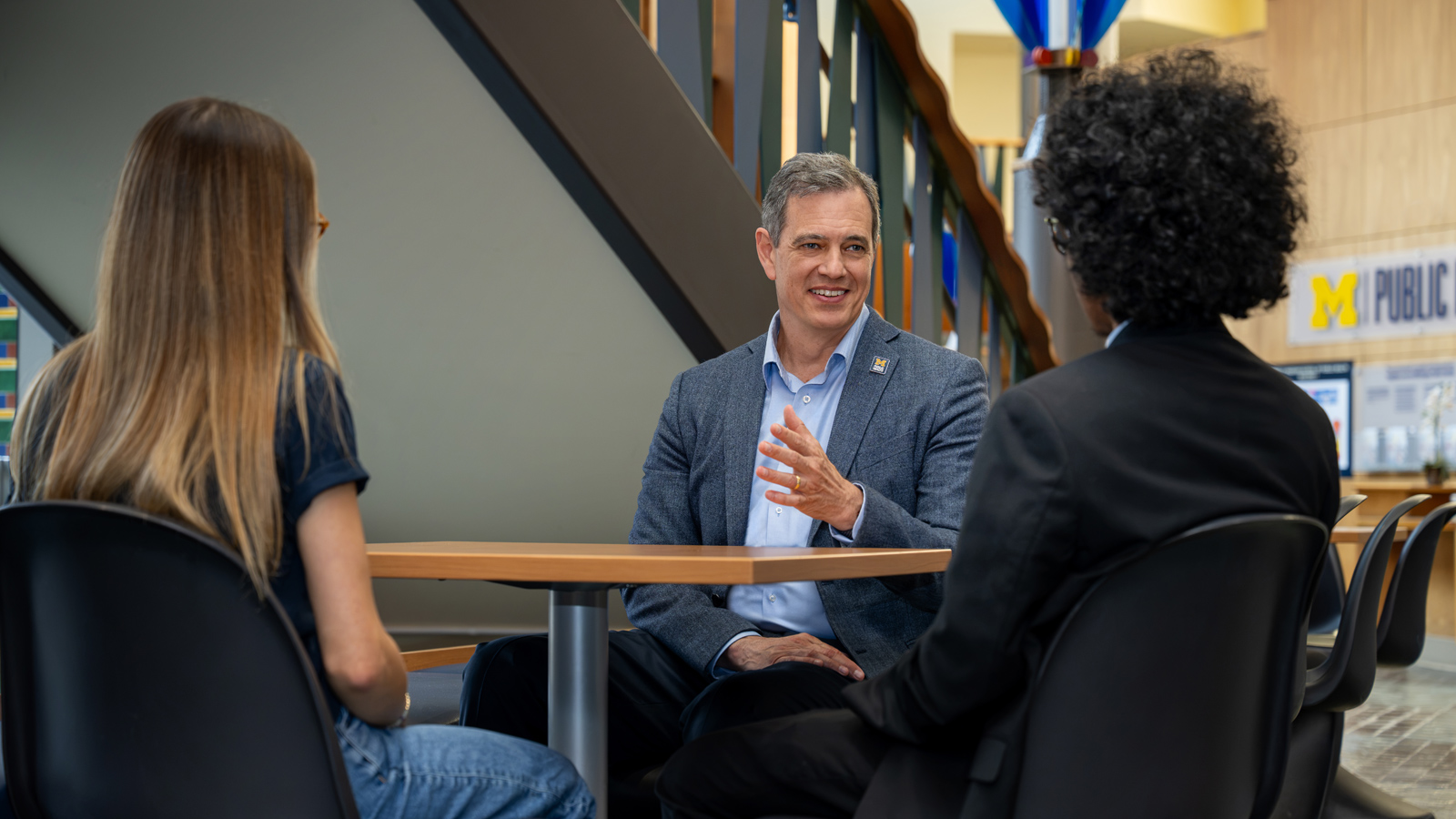 Dean Charles Holmes speaks with two students while seated at a table.