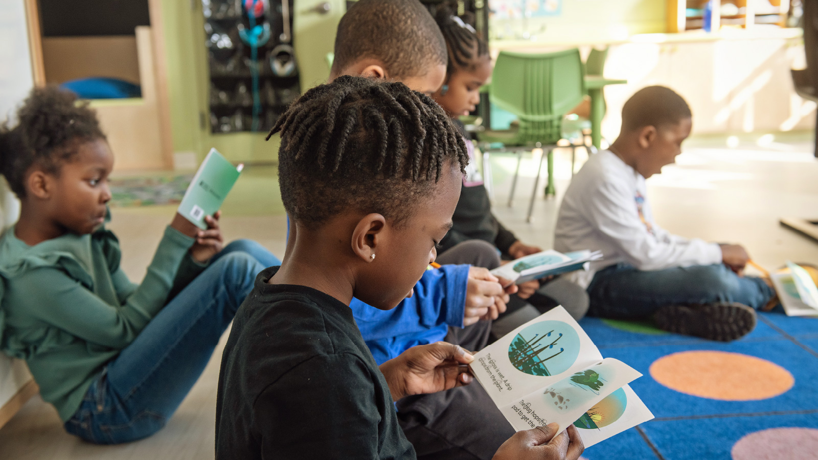 Young students sitting on the classroom carpet reading books.