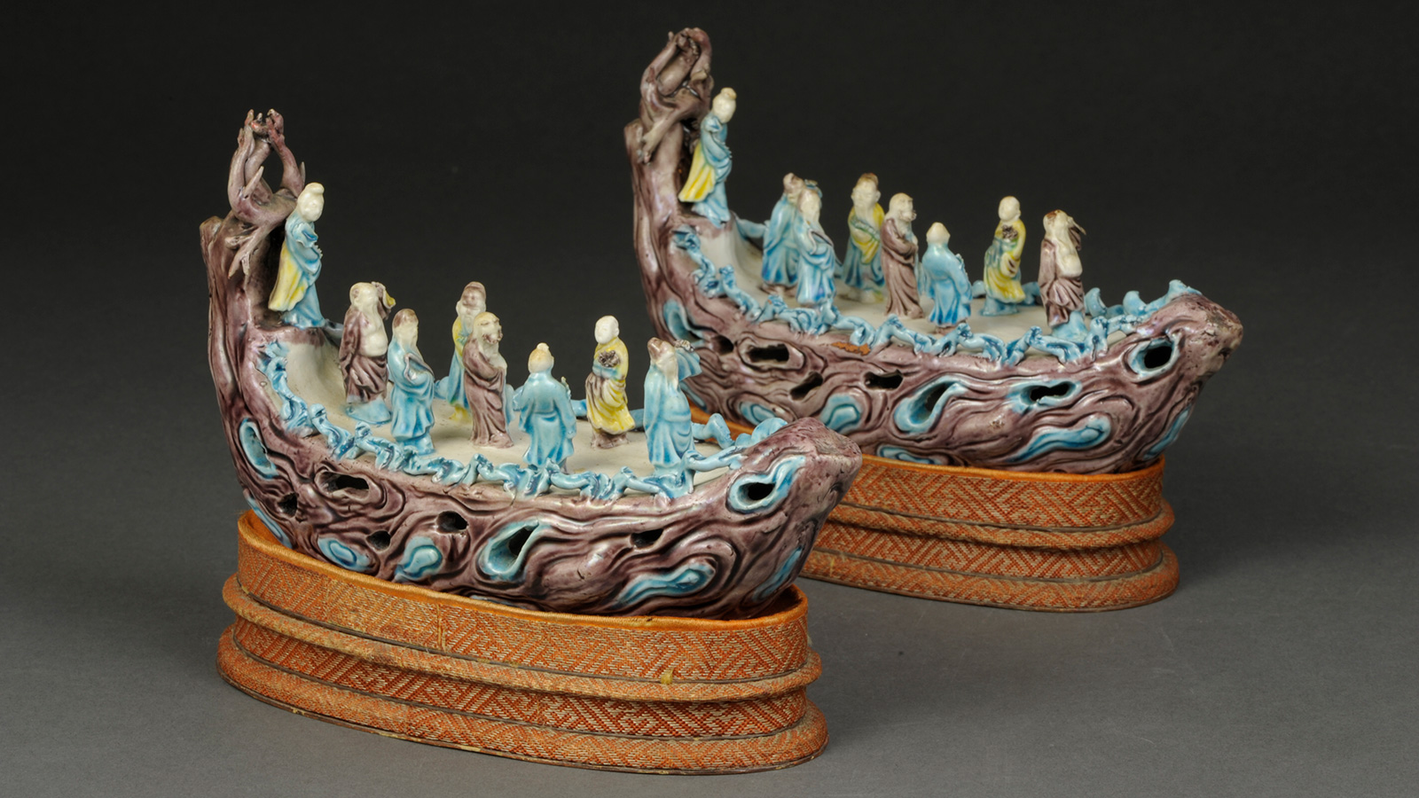 Two ornate miniature boat sculptures with small robed figures are displayed on patterned stands.