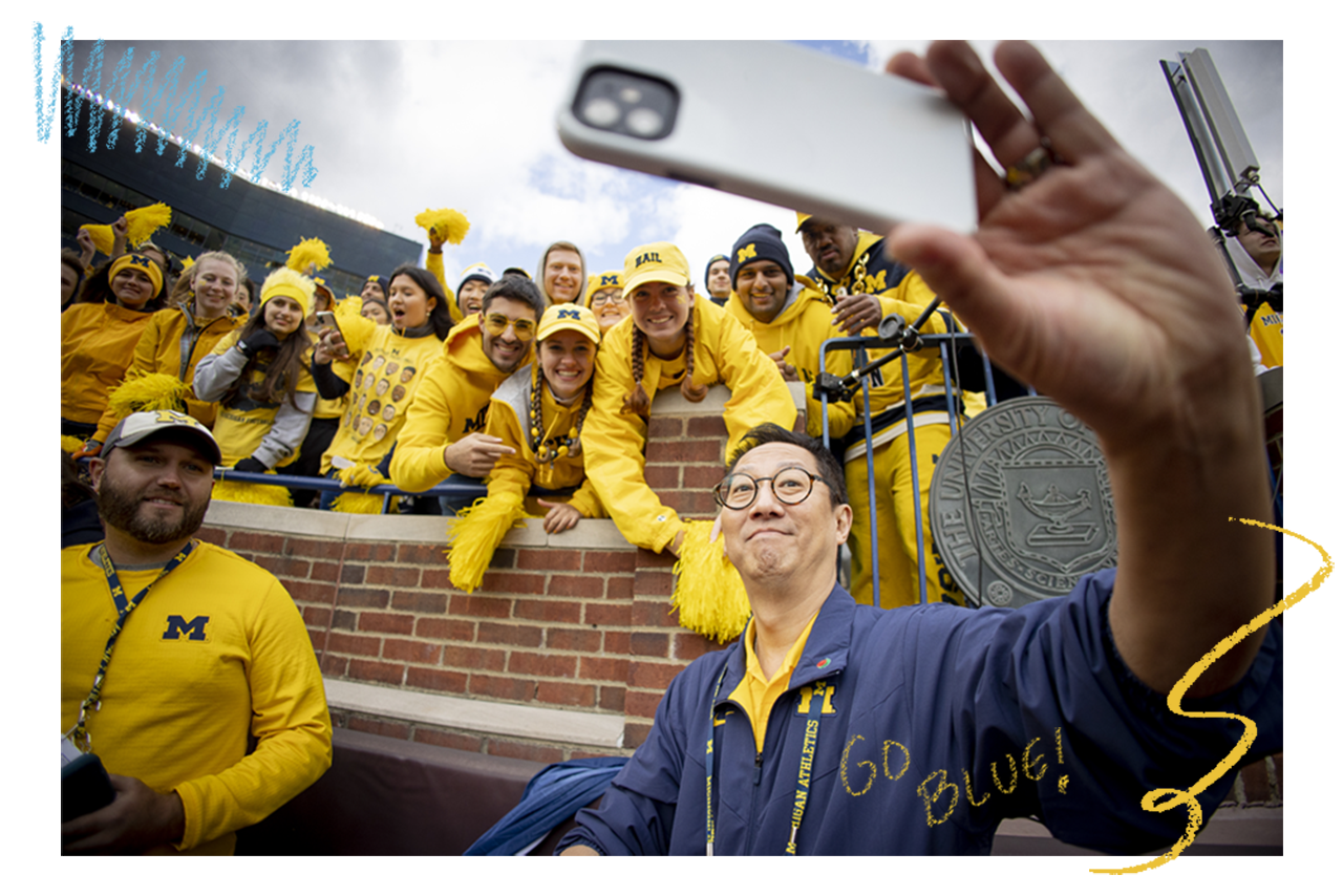 Enjoying his first Michigan football game at the Big House, President Ono takes a signature selfie with a crowd of cheering fans.