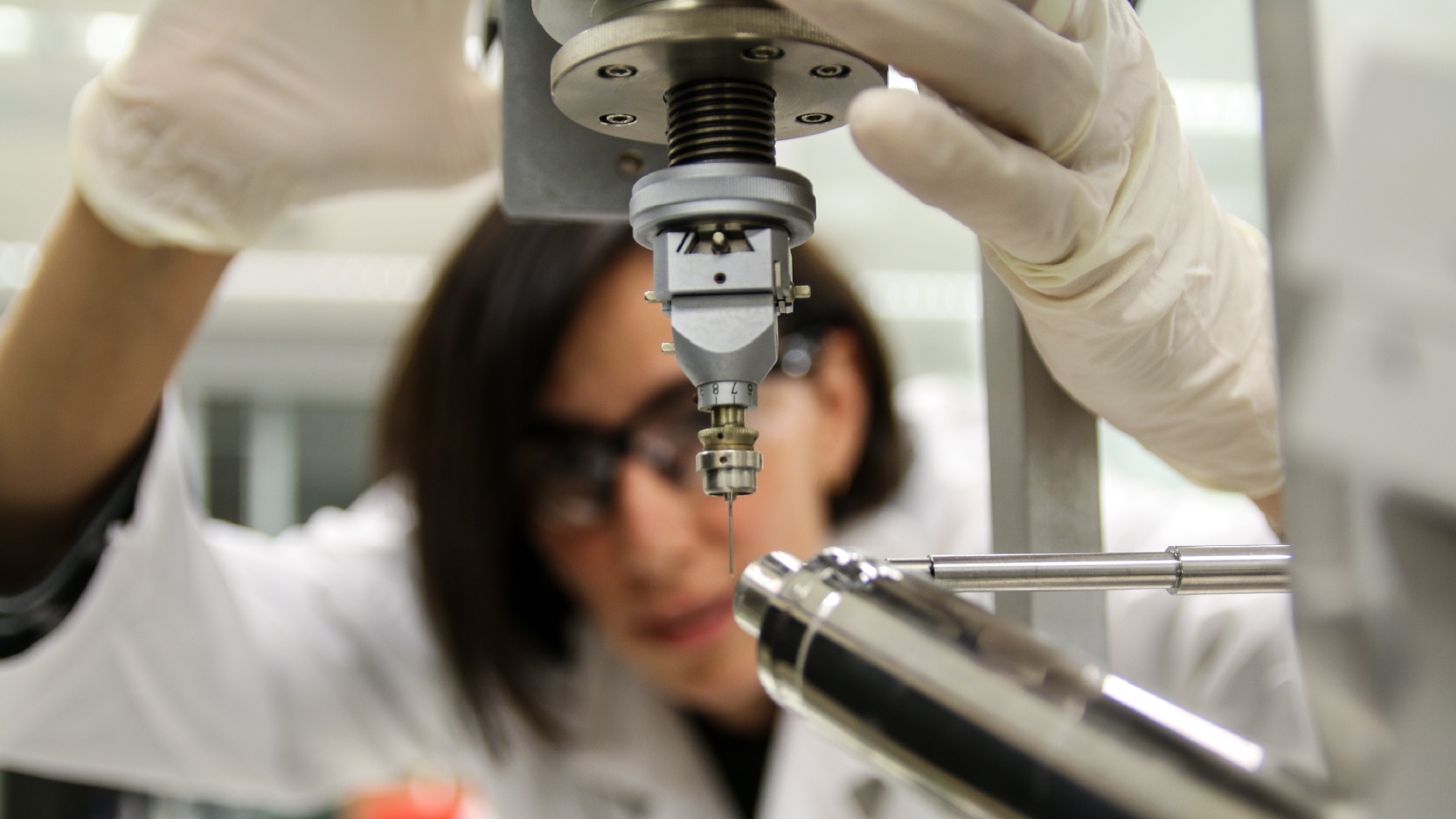 A woman in a lab coat and rubber gloves using a scientific instrument