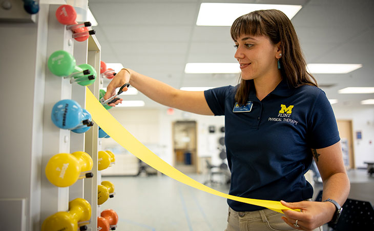 Rebecca James cutting an exercise band next to a rack of dumbbell weights.