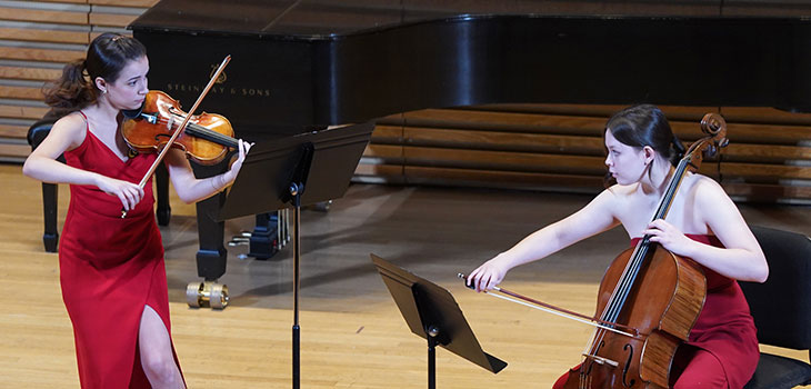 Two young women performing, one playing the violin and one playing the cello.