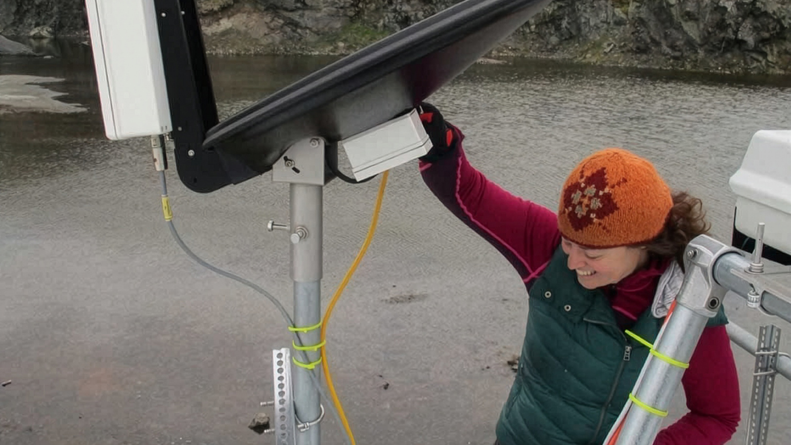  Claire Pettersen climbing down a ladder, holding onto a large radar she installed at a field site.