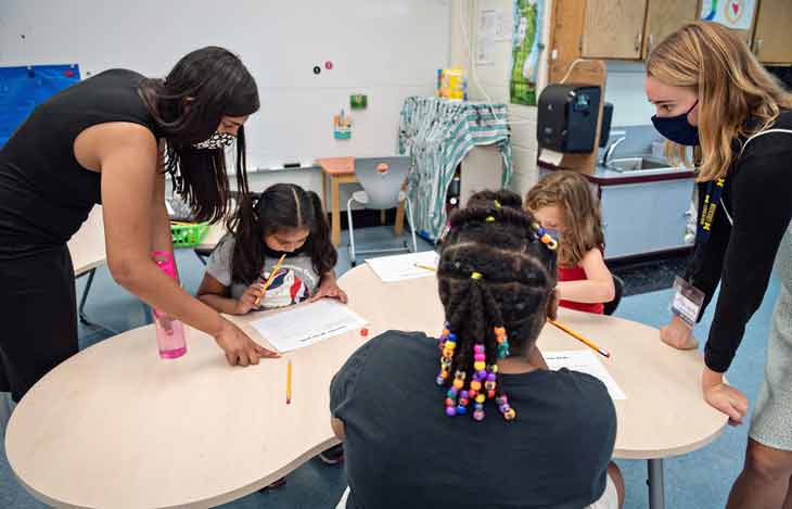 School of Education interns helping children play a learning game with dice, pencils, and paper.