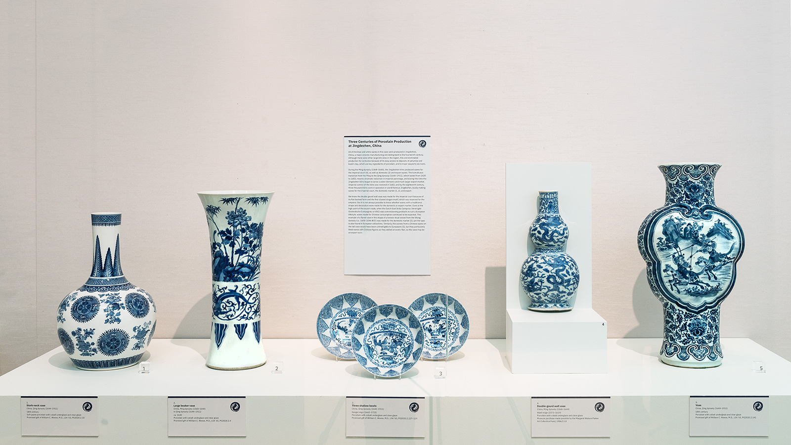 Blue-and-white ceramic vases and plates are displayed in a museum case with labels.