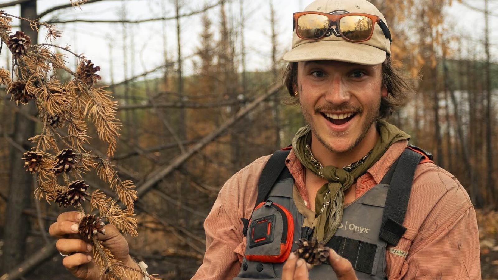 Kian McDonough out on the field holding a pine tree branch in one hand and a pine cone in the other hand