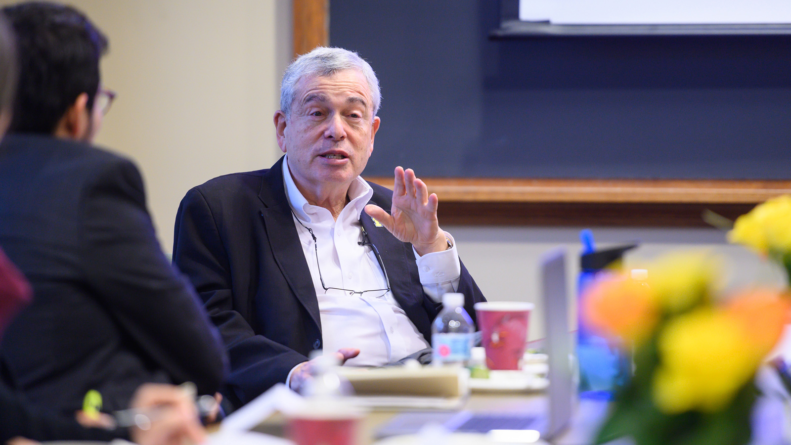 Ron Weiser seated at a table during a discussion, with a hand raised.