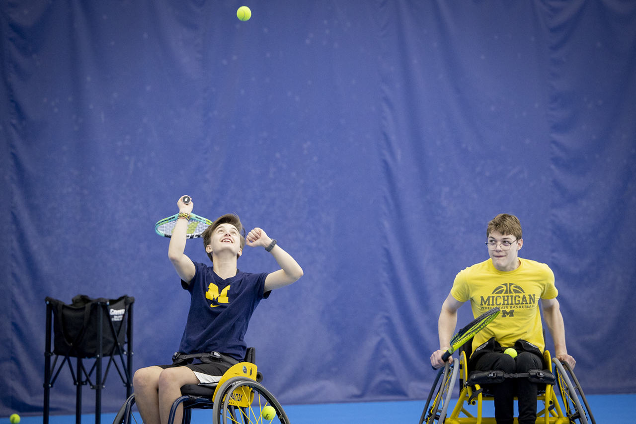 Two wheelchair tennis players holding tennis rackets, and one player is preparing to hit the tennis ball.