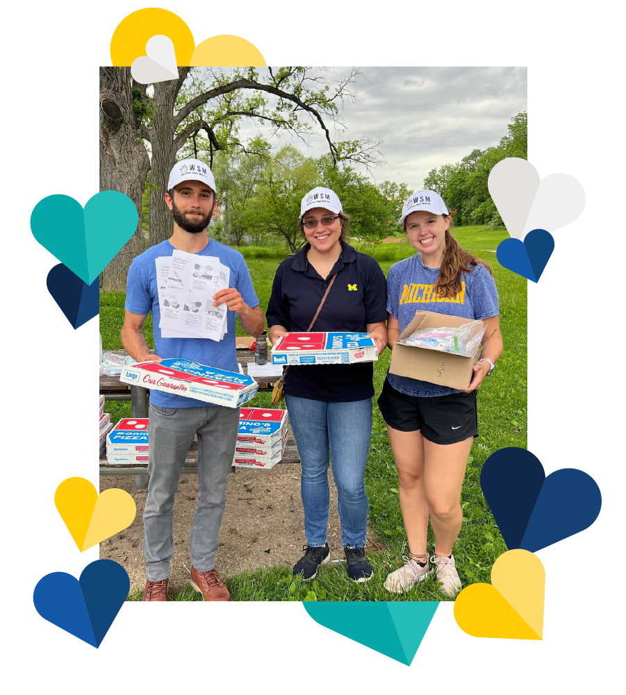 Wolverine Street Medicine members standing outside in a park. They are holding pizza boxes and a box of naloxone kits. Illustrations of hearts surround the photo.