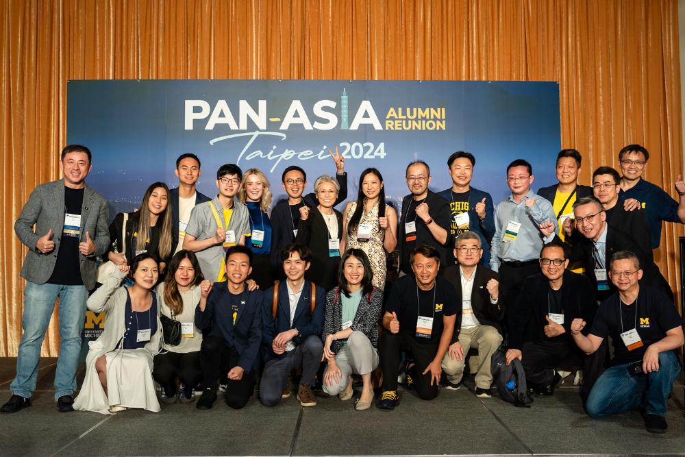 Cheering international alumni pose in from of a Pan Asia event banner.