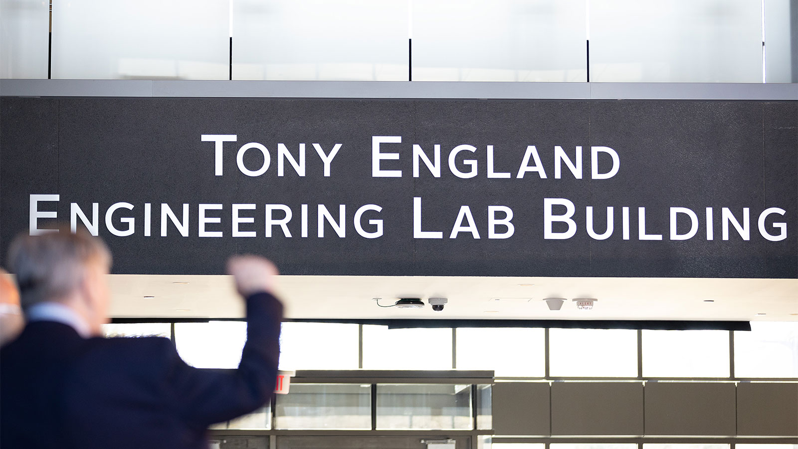 A sign saying Tony England Engineering Lab Building with a man in the foreground, seen from behind, with a raised arm.