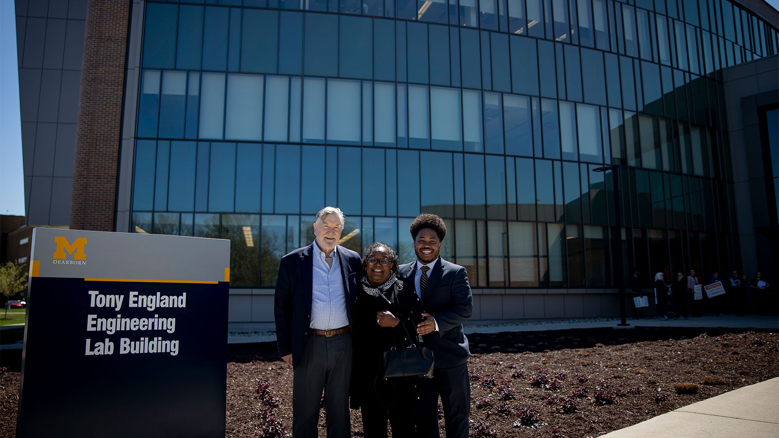 Man, woman, and young man standing in front of a building with a large glass wall and sign that says Tony England Engineering Lab Building. 