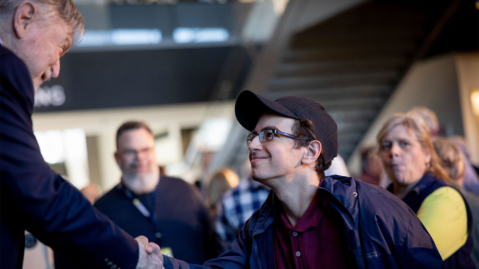 Man shaking hands with a young man, smiling, with people looking on.