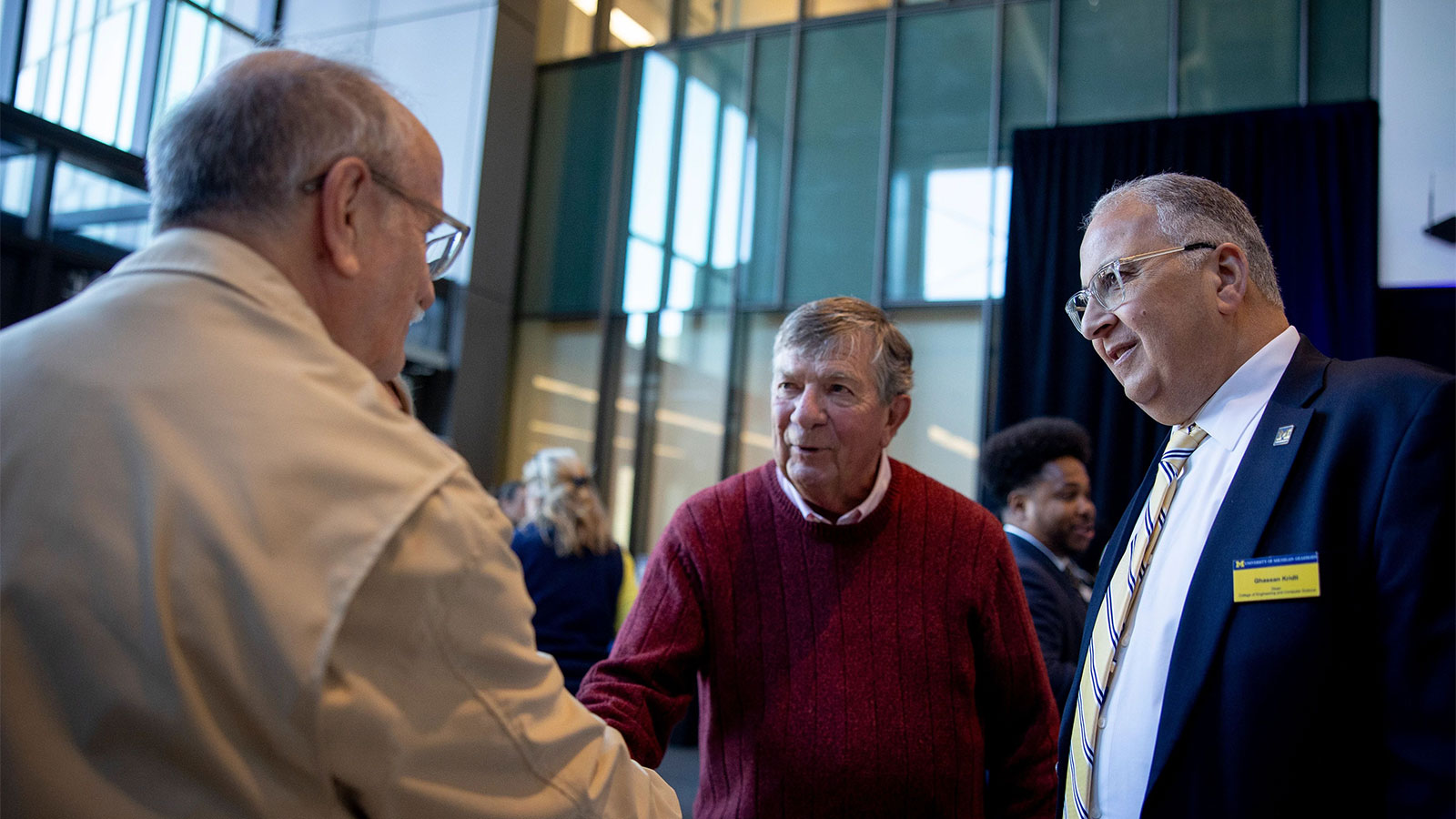 Three men greeting each other. Two are shaking hands.