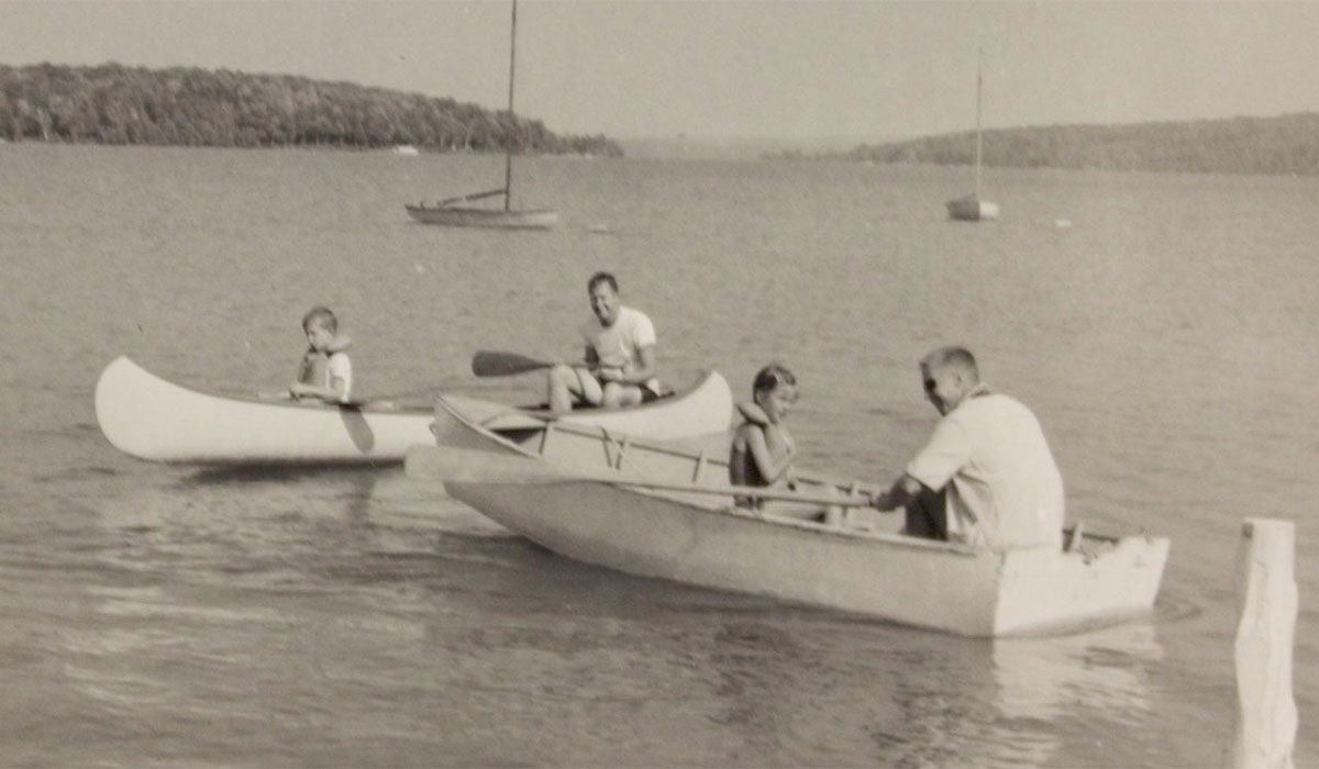 Historic photo from Camp Michigania with four people in two small boats on a lake. 