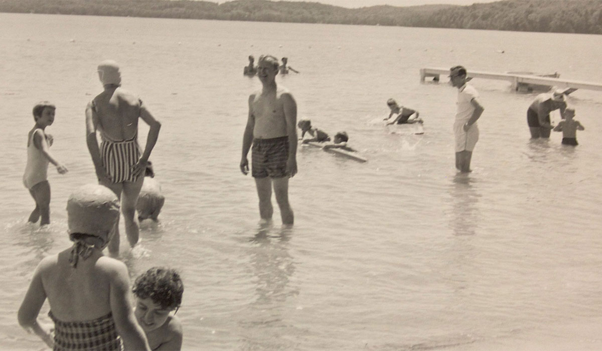 Historic photo of Camp Michigan where people are swimming and playing together in a lake.