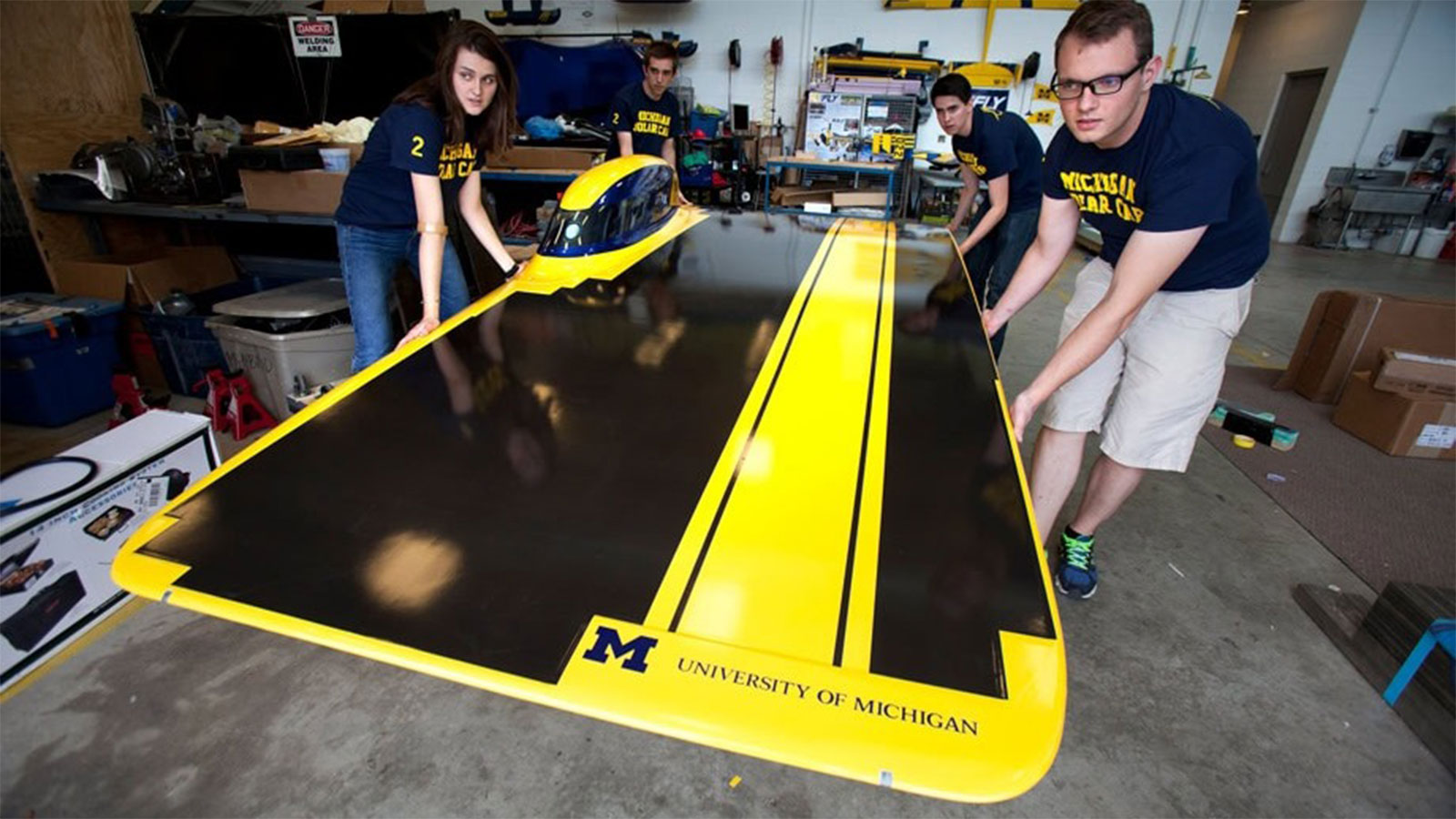 Four students carefully lift a solar car.