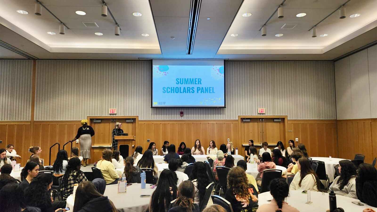 2024 Summer Scholars panel presentation to the 2024-2025 WISE RP cohort seated at tables. 