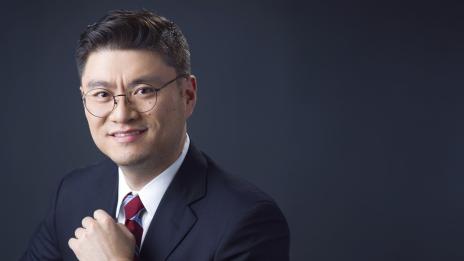 James Lu in a dark suit and red striped tie, posed against a plain dark background.