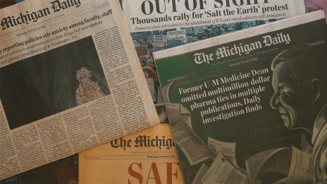 A scattered pile of The Michigan Daily newspapers featuring headlines about university policies and faculty news.