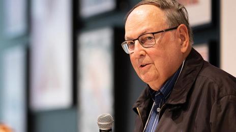 William Weese holds a microphone while speaking indoors.