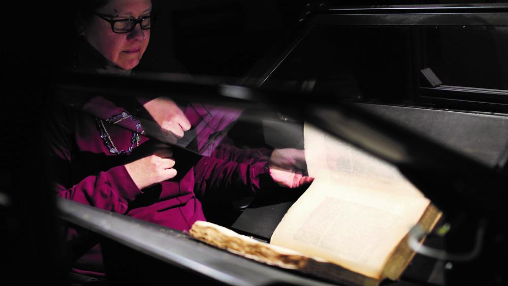 Woman holding glass panel to position page of a book on a scanner 